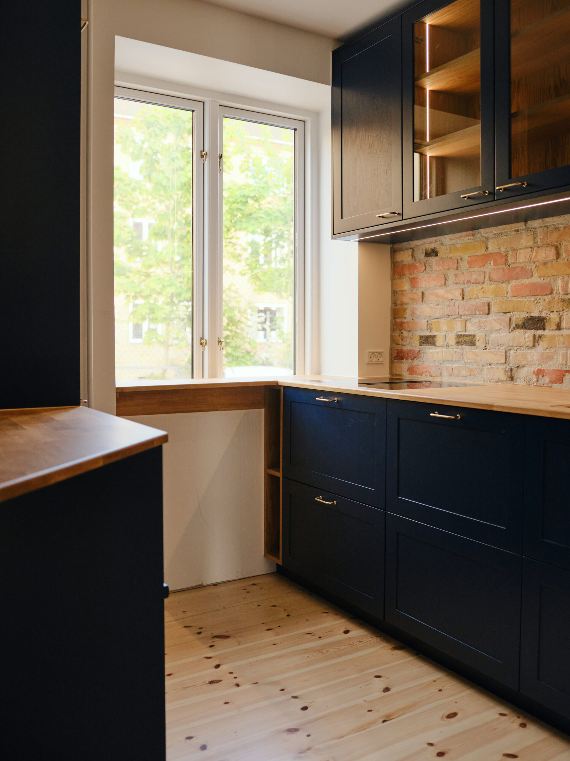 Bæredygtigt køkkendesign med mørke skabe og synligt murstensvæg.