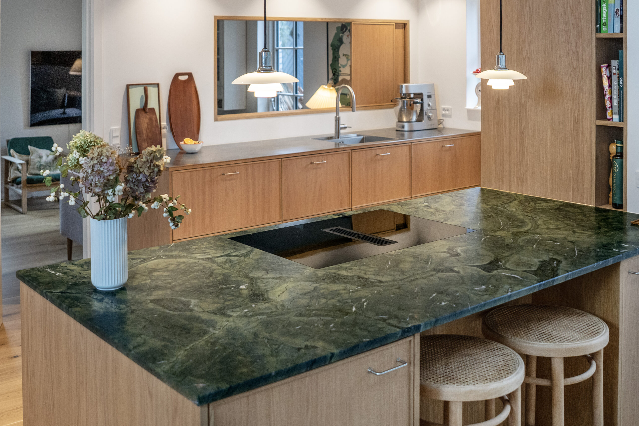 Bordplade i grøn marmor foran et moderne, lyst køkken i træ med barstole.