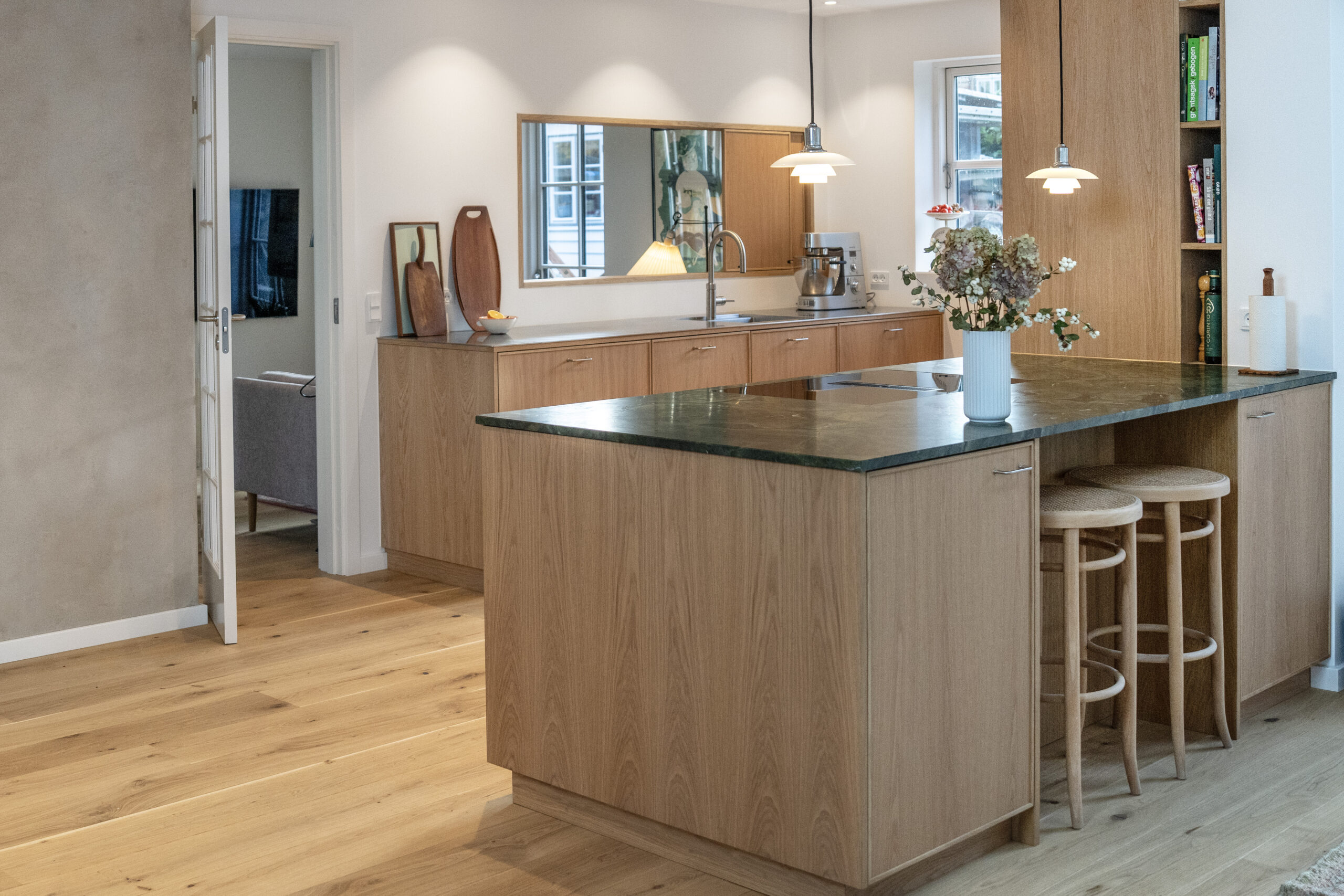 Elegant køkken med naturlige trælåger og grøn marmorbord. Moderne belysning og indretning skaber en varm atmosfære.