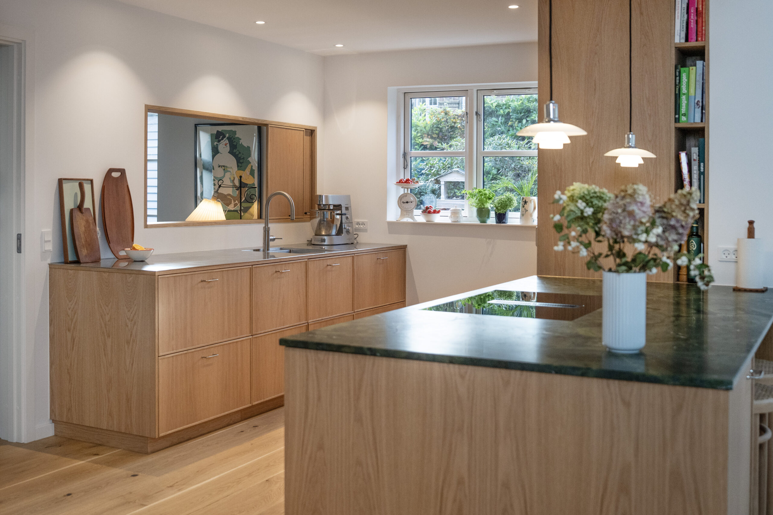 Elegante køkken i lyst træ med grøn marmorbord og moderne belysning, ideelt til moderne hjem.