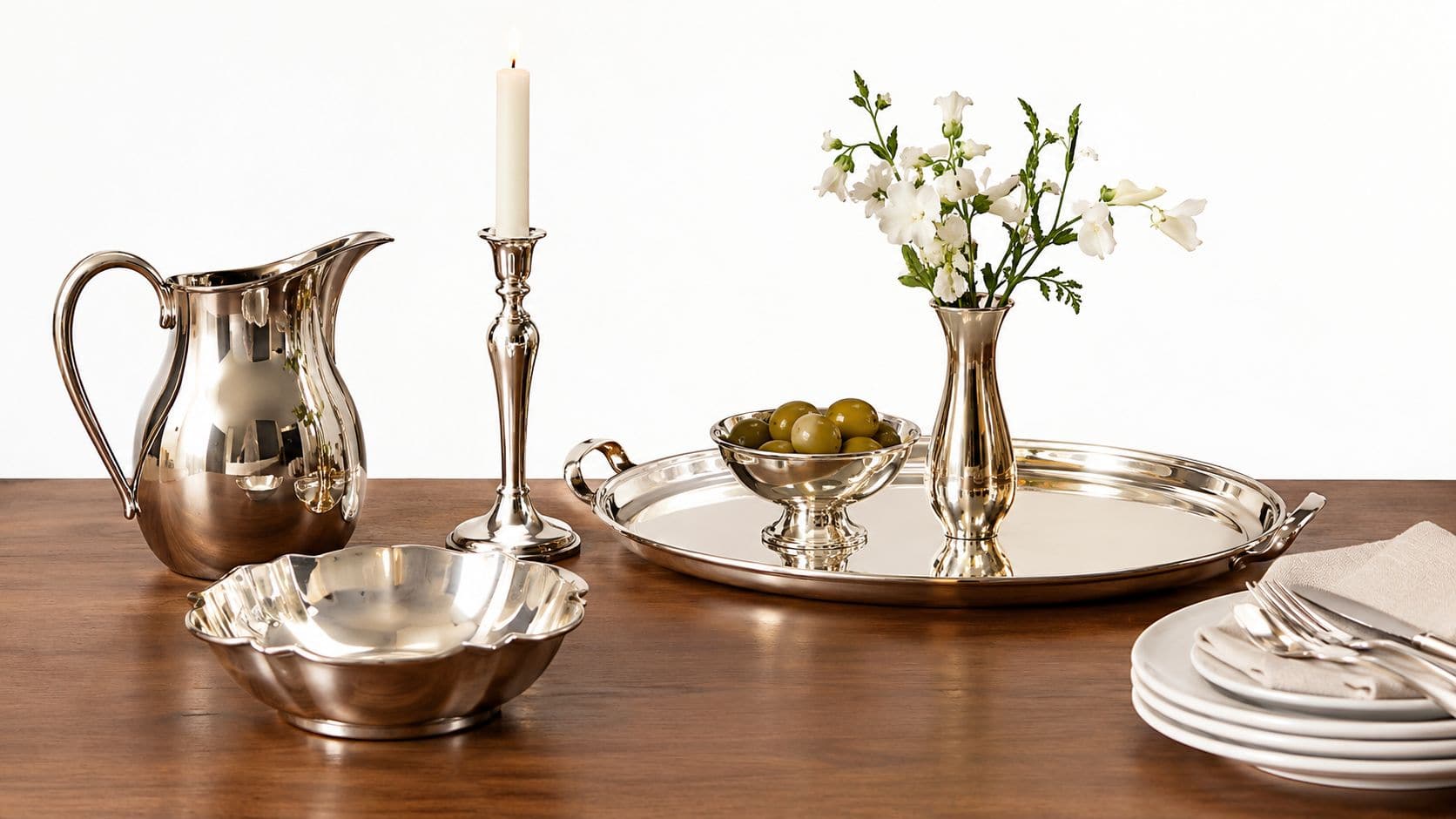 Et elegant borddækket setup med sølvbestik, en vase med blomster og en kande på en træoverflade.